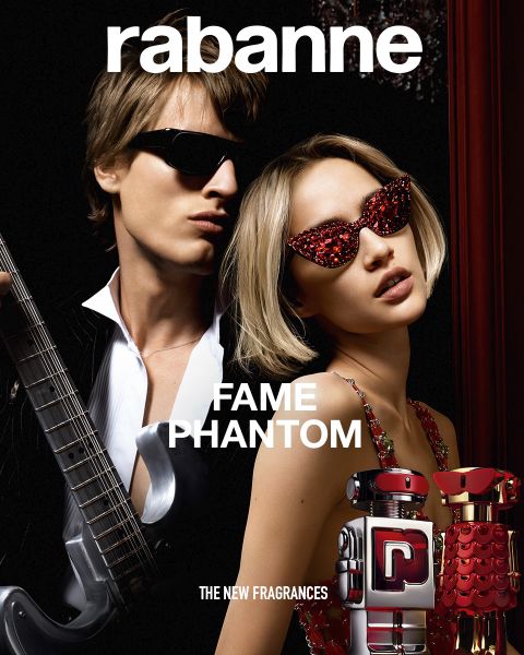 Due flaconi di profumo Rabanne Olympéa ABSOLU, uno nero e uno rosa, sono esposti davanti a un fiore bianco in fiore su uno sfondo scuro. Il testo recita: "Rabanne OLYMPÉA ABSOLU - LA NUOVA FRAGRANZA".