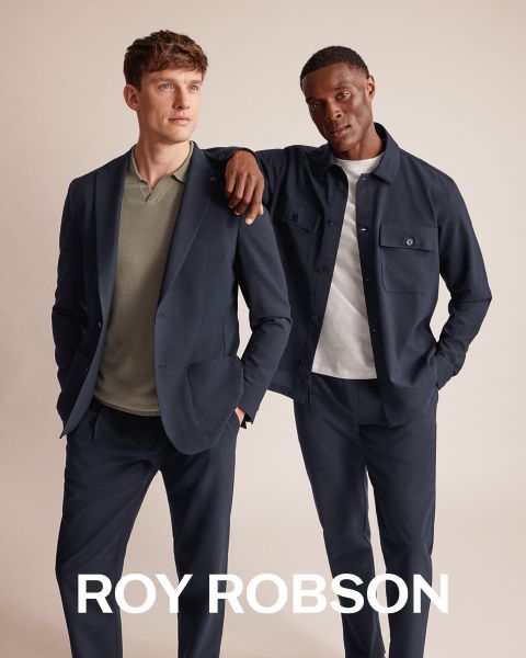 Un uomo è in piedi all'aperto di fronte a montagne innevate e indossa un cappotto pied-de-poule grigio, un maglione grigio e pantaloni grigi. Il testo "ROY ROBSON" appare nella parte inferiore dell'immagine.