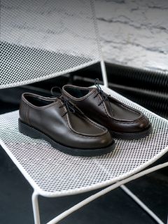 Persona in jeans arrotolati in piedi su un terreno sabbioso vicino a cactus, indossa scarpe da ginnastica bianche con accenti beige e marroni e un logo a "V" sul lato.