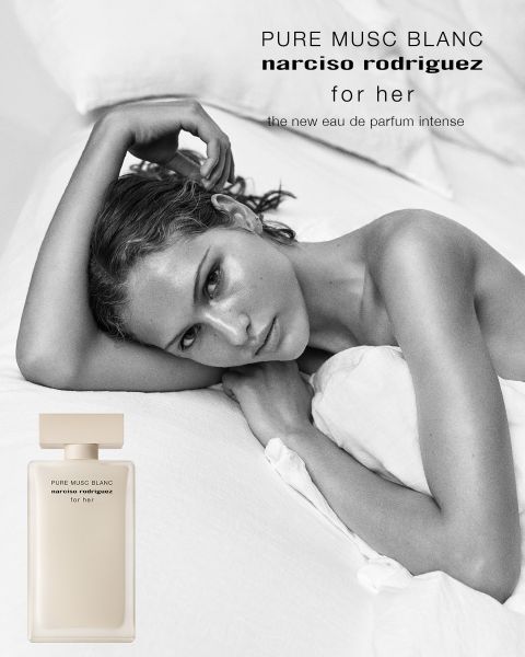 Una donna con capelli castani ricci posa di profilo accanto a un flacone di profumo rosa con la scritta "all of me narciso rodriguez floral". Il testo sopra recita "narciso rodriguez" e sotto: "La nuova eau de parfum floreale".