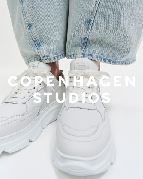 Primo piano di scarpe da ginnastica bianche con suole spesse indossate da una persona che indossa jeans azzurri. Il testo "COPENHAGEN STUDIOS" è sovrapposto all'immagine.