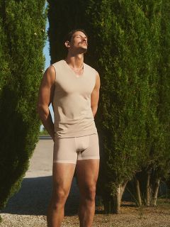 Una donna in abito rosso e occhiali da sole a forma di cuore è seduta su una sedia bianca, circondata da fiori colorati, tra cui rose, margherite e gigli. L'ambiente sembra essere un'area esterna notturna.