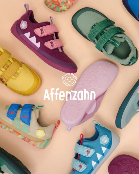 Un bambino con un vivace maglione arancione e pantaloni a righe è seduto su una superficie colorata e indica un aeroplanino di carta in stile fumetto nel cielo. Sorride ed è circondato da nuvole soffici. Nell'angolo c'è scritto "Affenzahn".