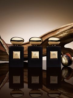 Sono esposti sei eleganti flaconi di profumo con lisci tappi dorati. Sono disposti sopra e intorno a un blocco dorato e presentano varie etichette con le scritte "OUD", "SNAKE" e "OUR", ciascuna con elaborati motivi neri e dorati su un delicato sfondo grigio.