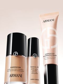Tre flaconi di profumo su una base dorata davanti a uno sfondo bianco ondulato e strutturato. I flaconi sono neri con etichette dorate e tappi ovali lisci e scuri.