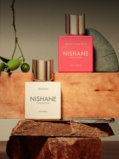 Un flacone del profumo "Hundred Silent Ways" di Nishane con un tappo dorato che si riflette in basso e uno sfondo sfocato rosso e nero.