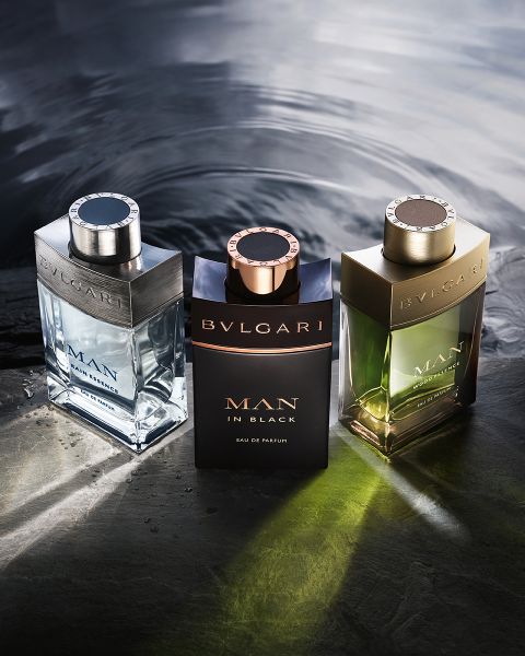 Una donna in abito bianco si appoggia sullo sfondo di un'architettura moderna sotto un cielo blu. In primo piano, due flaconi del profumo Bvlgari Omnia Crystalline, che presentano tonalità chiare e ambrate.