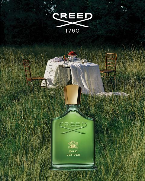 Un flacone bianco di profumo Creed Silver Mountain Water giace nella neve con cime innevate sullo sfondo sotto un cielo blu.