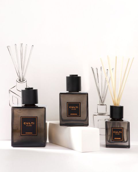 Un'elegante presentazione di prodotti profumati per ambienti di Culti Milano, tra cui candele, un diffusore con bastoncini e flaconi, tutti in contenitori verde scuro, su uno sfondo color oliva con il logo di Culti Milano sottostante.