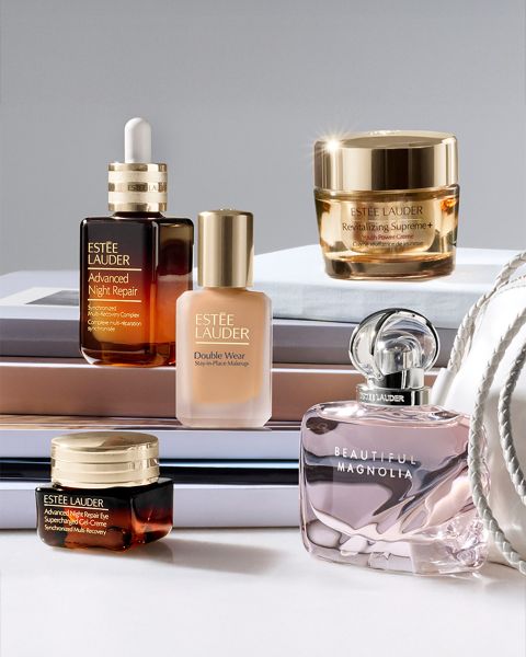 Una donna con i capelli lunghi posa con una bottiglia di Estée Lauder Advanced Night Repair in primo piano. Sullo sfondo si vede un paesaggio urbano notturno. Un testo tedesco descrive i vantaggi del prodotto per la cura della pelle.
