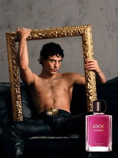 Una bottiglia di JOOP! Homme Le Parfum è tenuta davanti a uno sfondo sfocato con un fiore di iris viola. Il logo dorato di "JOOP!" è chiaramente visibile in alto. L'immagine trasmette eleganza e lusso.