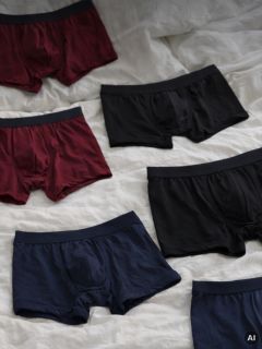 Sei paia di boxer da uomo nei colori nero, bordeaux e blu navy sono stesi su un panno bianco.