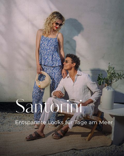 Una donna in un vestito floreale blu sta accanto a un uomo seduto in abiti bianchi. Il testo recita: "Santorini - Look rilassati per giornate al mare."