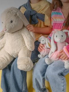 Un ragazzo sorridente con i capelli biondi è seduto in una casa e abbraccia un grande orsacchiotto beige. Indossa una maglietta a maniche lunghe bianca e nera e pantaloni chiari.