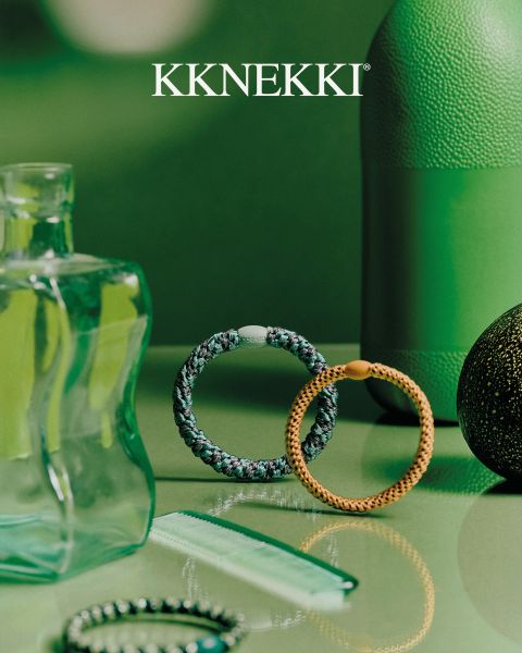 Una persona con un maglione blu navy e jeans tiene una spazzola per capelli blu dietro la schiena e indossa braccialetti di perline turchesi. Sopra il logo "KKNEKKI".