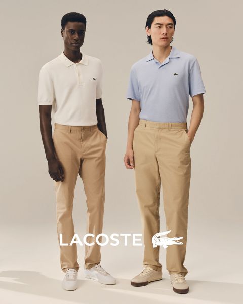 Quattro modelli posano all'aperto in abiti Lacoste con un cielo blu sullo sfondo. Da sinistra a destra: una persona in trench, una persona in maglione e pantaloni, una persona in gilet e gonna e una persona in tuta da ginnastica. Il logo Lacoste si trova in basso.