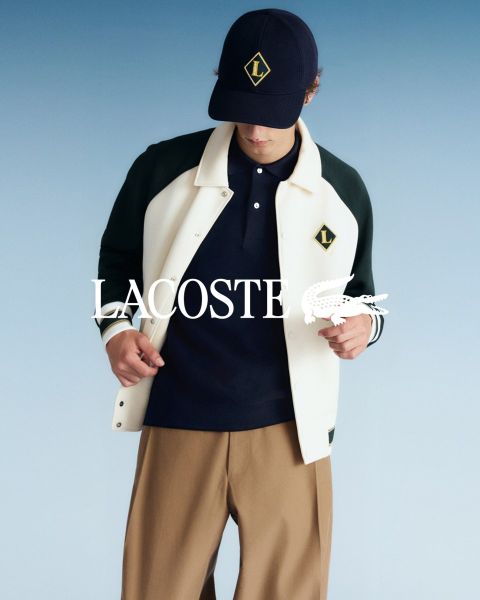 Quattro modelli posano all'aperto in abiti Lacoste con un cielo blu sullo sfondo. Da sinistra a destra: una persona in trench, una persona in maglione e pantaloni, una persona in gilet e gonna e una persona in tuta da ginnastica. Il logo Lacoste si trova in basso.