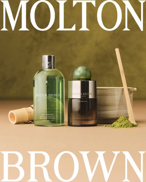 Disposizione piatta di diverse bottiglie e contenitori Molton Brown su uno sfondo chiaro, con il testo "Molton Brown London, Fragranza distintiva, Made in England" al centro. Accenti sferici in vetro sparsi ovunque.