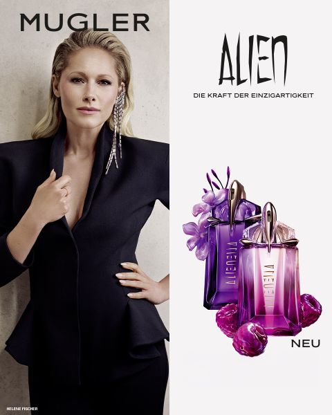 Una donna con una pelle scura e radiosa e lisci capelli neri posa davanti a uno sfondo viola. Davanti a lei ci sono due flaconi di profumo Alien di Mugler. Il testo recita "MUGLER" e "ALIEN EXTRA INTENSE LE FRAGRANZE RICARICABILI".