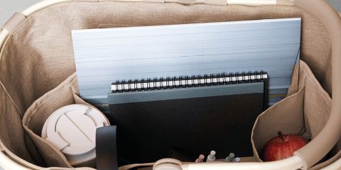 Una persona con lunghi capelli rossi, che indossa una camicia azzurra e pantaloni bianchi, si rilassa nell'erba e tiene in mano una borsa fantasia. Si trova all'aperto in un campo soleggiato con vista sulle colline in lontananza. La parola "Reisenthel" è visibile in rosso.