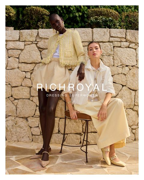 Una donna in camicia azzurra e pantaloni grigi si tiene una palla di neve davanti a un occhio. Posa in una stanza con pareti in legno e un poster di sci, e indossa grandi orecchini. Il testo recita "RICHROYAL DRESSING SUPERWOMEN".