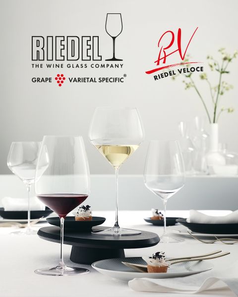 Sei colorati bicchieri di cristallo con intricati motivi intagliati sono disposti su una superficie di marmo scuro. Sopra spicca il logo Riedel con il marchio e il simbolo di un bicchiere da vino.