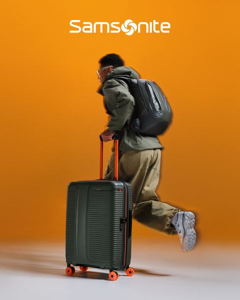 Valigia Samsonite verde chiaro con motivo strutturato e quattro ruote. Il manico è estraibile. Il grande logo "Samsonite" è disposto orizzontalmente sulla valigia. Lo sfondo ha un design ondulato verde e bianco.