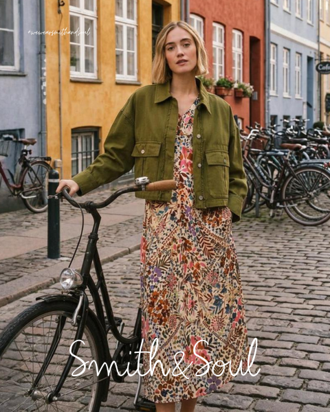 Una donna con una camicia rosa e un cardigan con pantaloni bianchi posa davanti a uno sfondo bianco. Il testo recita "Smith & Soul" in basso.