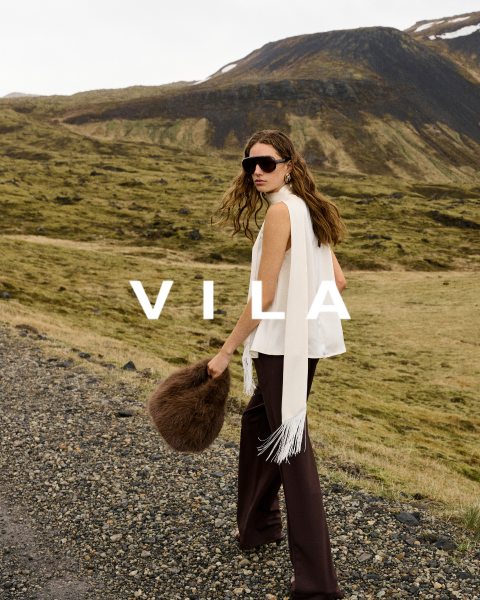 Cinque donne in abbigliamento casual, tra cui jeans e top in colori neutri, sono in piedi vicine e sorridono davanti a uno sfondo semplice. Il testo sovrapposto recita "Vila Clothes".