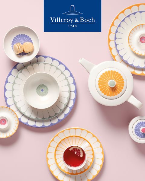 Una mostra di cucine espone una ciotola nera con piccole fruste su un vassoio rettangolare. Accanto si trova un piatto con coperchio di vetro, su cui sono disposti formaggio ed erbe fresche. In alto spicca il logo di Villeroy & Boch.