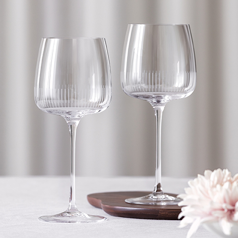 Un'elegante composizione di tre raffinati bicchieri da cocktail su un tavolo scuro con un vaso di ceramica contenente rami frondosi. Ogni bicchiere contiene una bevanda limpida e guarnizioni. La scena è illuminata da una luce calda e ha uno sfondo dorato.