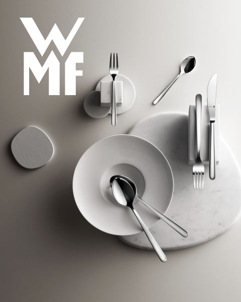 Una pentola piena di fichi, more e guarnizioni aromatiche è appoggiata su un tagliere di legno scuro. Sopra la pentola si vede il logo WMF. Lo sfondo è una superficie scura strutturata.