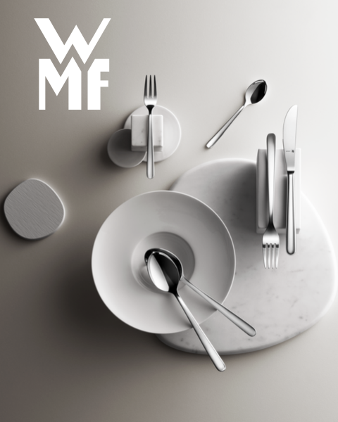 Una pentola piena di fichi, more e guarnizioni aromatiche è appoggiata su un tagliere di legno scuro. Sopra la pentola si vede il logo WMF. Lo sfondo è una superficie scura strutturata.