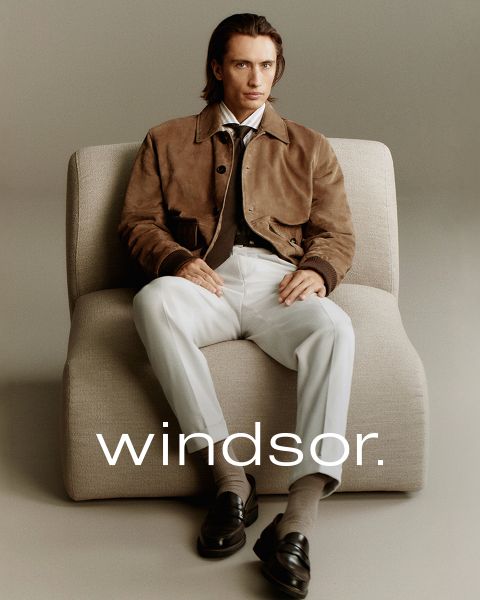 Un uomo con un cappotto marrone e una donna con un cappotto e una sciarpa color crema sono in piedi all'aperto con le montagne sullo sfondo. La parola "windsor." è visibile nella parte inferiore dell'immagine.