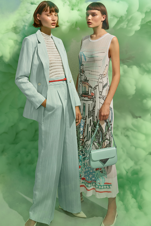 Due modelle posano davanti a uno sfondo di fumo verde. Una indossa un abito azzurro con un top a motivi bianchi, l'altra un abito senza maniche con motivi grafici. Entrambe hanno i capelli corti e scuri e indossano accessori pastello abbinati.
