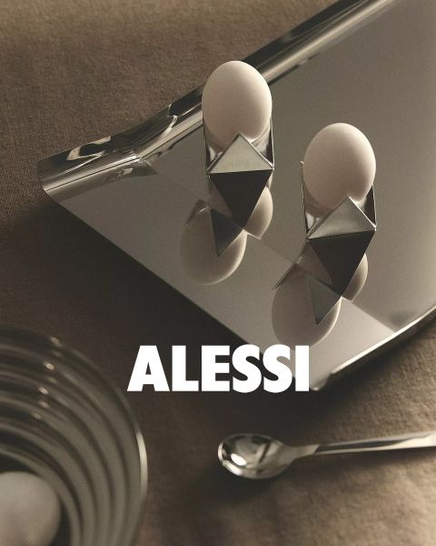 Due moderni portauovo geometrici con uova sono posizionati su un vassoio riflettente, insieme a una ciotola di vetro e un cucchiaio. In basso al centro dell'immagine si legge "ALESSI" in grassetto.