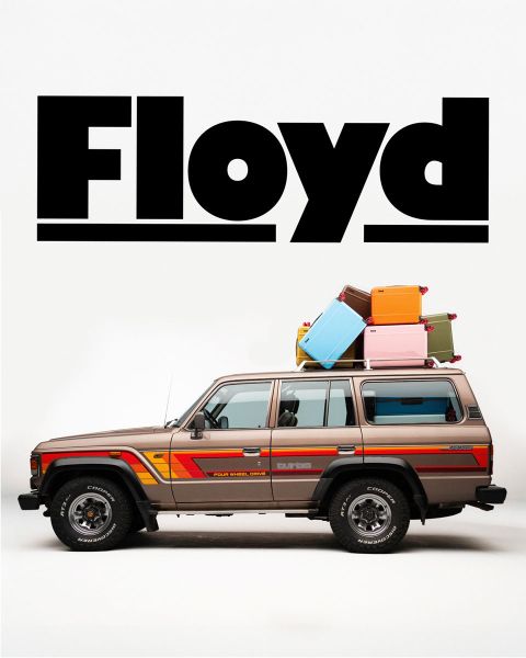 Un SUV d'epoca in stile retrò con bagagli sul tetto è parcheggiato su uno sfondo bianco. Sopra il veicolo campeggia la parola "Floyd" in grassetto nero.