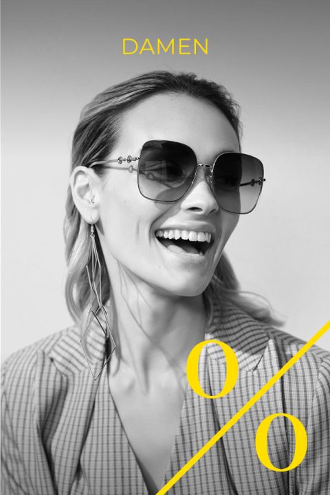 Foto in bianco e nero di una donna sorridente con grandi occhiali da sole e lunghi orecchini, vestita con un blazer a quadri. La parola "DONNE" e un grande simbolo di percentuale giallo sono sovrapposti all'immagine.
