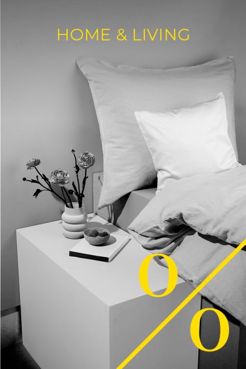 Una moderna scena di camera da letto con un letto, cuscini grandi e piccoli, un vaso di fiori, un libro e una ciotola in bianco e nero. Le parole "CASA & ARREDAMENTO" e un grande simbolo di percentuale giallo sono sovrapposti all'immagine.