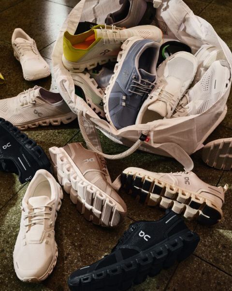 Una varietà di scarpe da corsa On di diversi colori sono sparse sul pavimento e fuoriescono da una borsa bianca, mettendo in mostra le loro inconfondibili suole ammortizzate.