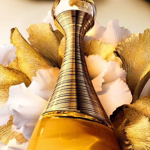 Un primo piano di un elegante flacone di profumo dorato, circondato da petali bianchi bordati d'oro, che crea una composizione lussuosa e artistica.