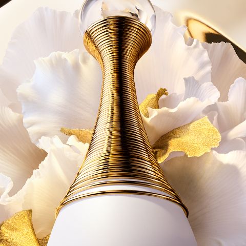 Un primo piano di un lussuoso flacone di profumo con un collo dorato avvolto a spirale, su uno sfondo di morbidi petali bianchi, accentuato da un tocco d'oro.