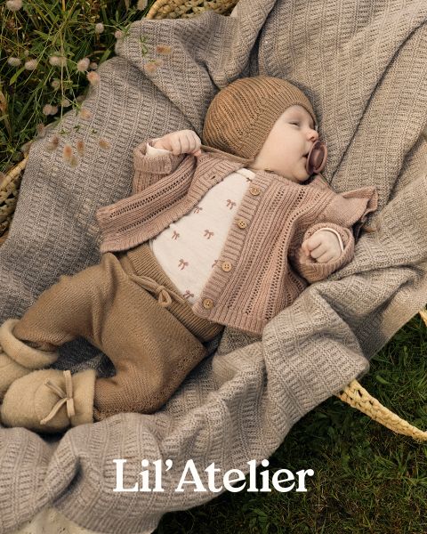 Un neonato che indossa un cappello, un cardigan e dei pantaloni di maglia marroni è adagiato in un cesto all'aperto su una coperta beige strutturata. Il bambino ha un ciuccio e dei piedini. Il testo in basso recita "Lil' Atelier".