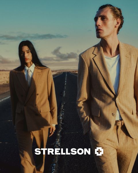 Un uomo e una donna in eleganti abiti marroni camminano lungo una strada vuota al tramonto. Il logo Strellson appare nella parte inferiore dell'immagine.