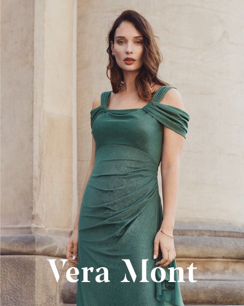 Una donna in un abito senza spalline verde luccicante è in piedi davanti a un muro di pietra. Il testo "Vera Mont" appare nella parte inferiore dell'immagine.