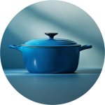 Ein runder, blau emaillierter gusseiserner Dutch Oven mit Deckel und Griffen steht auf einer passenden blauen Fläche, die von weichem, natürlichem Licht beleuchtet wird.