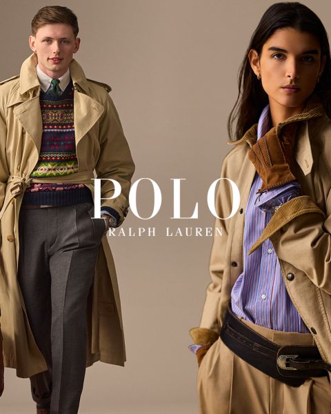 Un uomo e una donna indossano eleganti trench Ralph Lauren. L'uomo abbina il suo cappotto a un maglione colorato e pantaloni grigi, mentre la donna indossa una camicia a righe, guanti marroni e una cintura larga. "POLO RALPH LAUREN" è mostrato in caratteri bianchi.