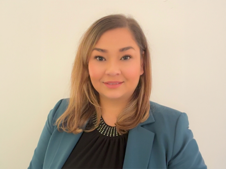 Donna con capelli castano chiaro lunghi fino alle spalle, che indossa un blazer verde acqua e un top nero, sorride davanti a uno sfondo semplice e luminoso.