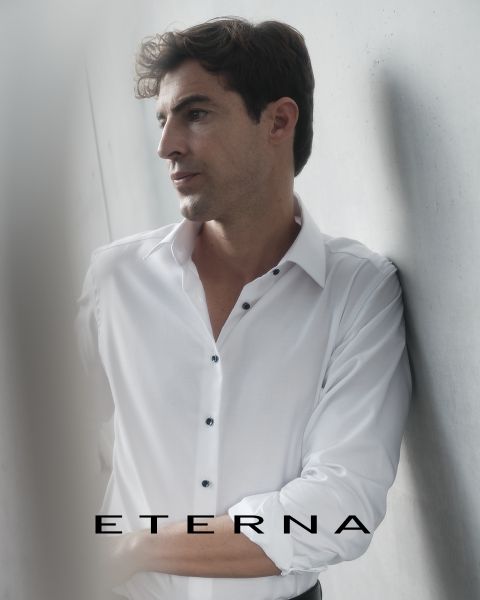 Un uomo in camicia bianca è appoggiato a un muro chiaro e guarda pensieroso di lato. Nella parte inferiore dell'immagine c'è la parola "ETERNA".