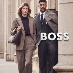 Una donna in tailleur beige e un uomo in abito grigio sono in piedi accanto al logo BOSS.